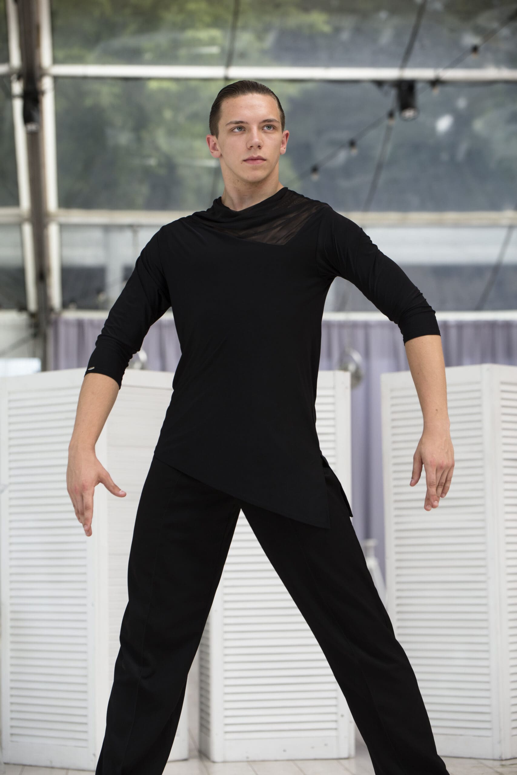 Male dancer wearing a black performance shirt and trousers in a dance studio.