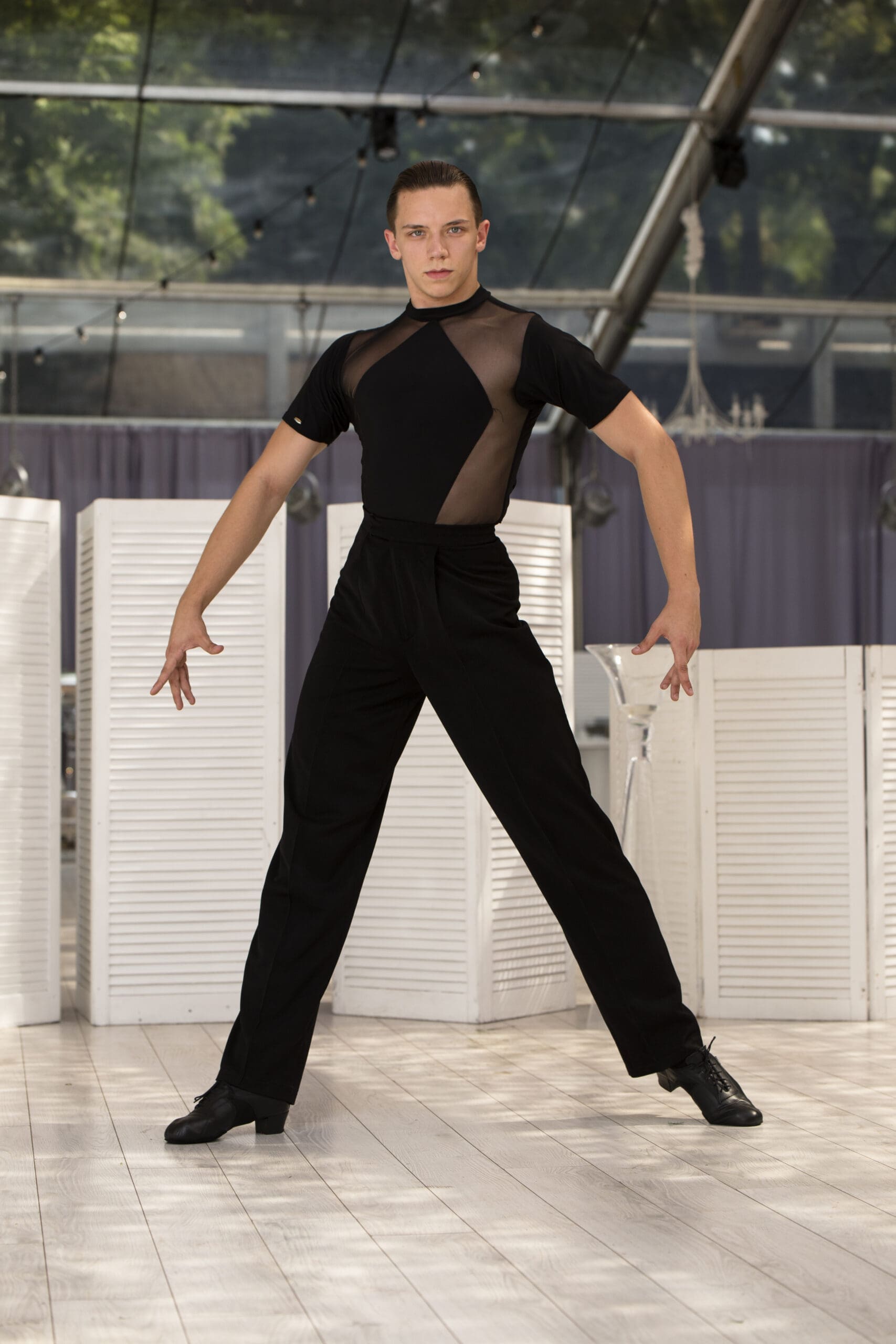 Male dancer showcasing a sophisticated black outfit with mesh detailing, ideal for ballroom and Latin dance.