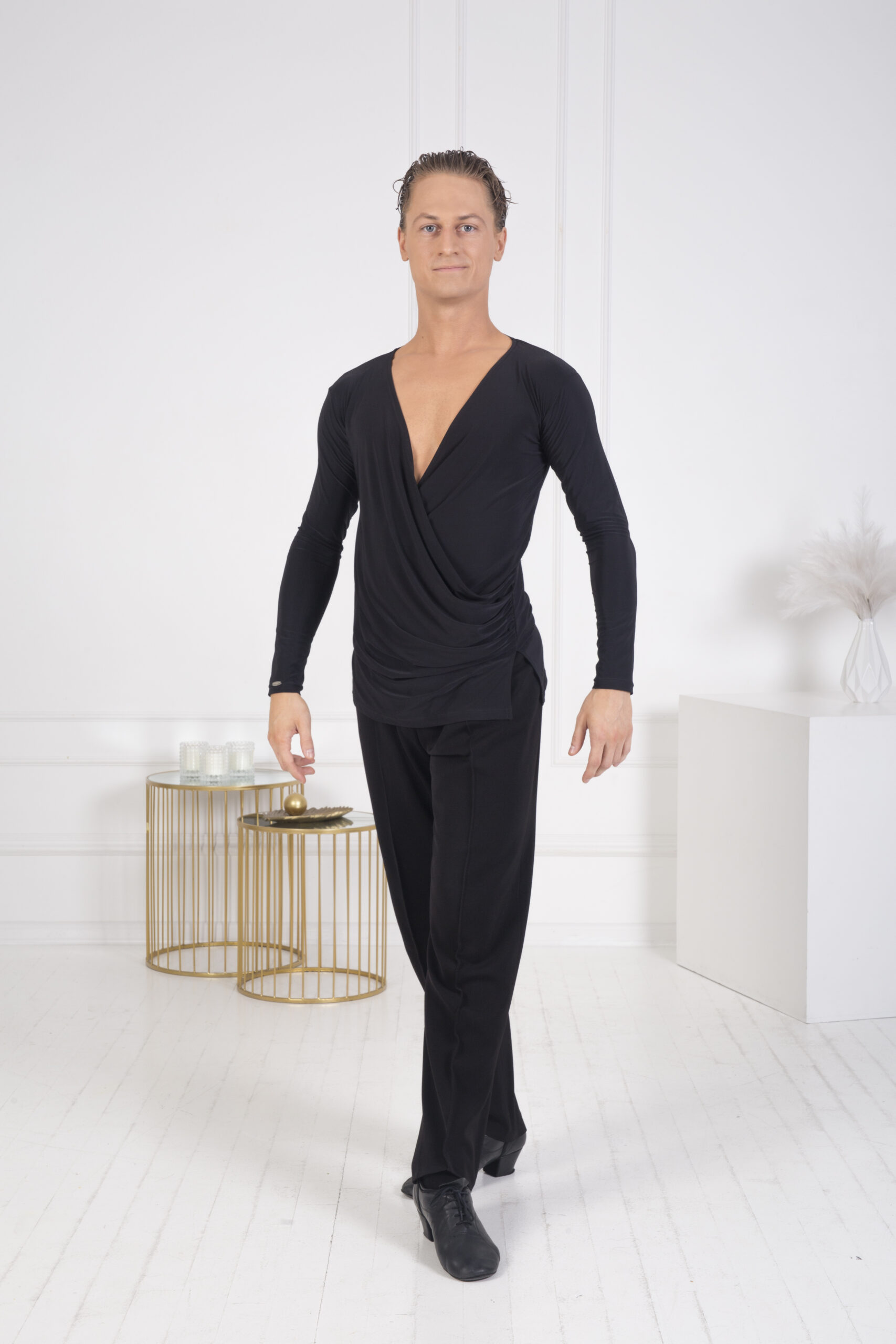 A male dancer wearing a stylish black performance outfit with a deep V-neck and matching trousers.
