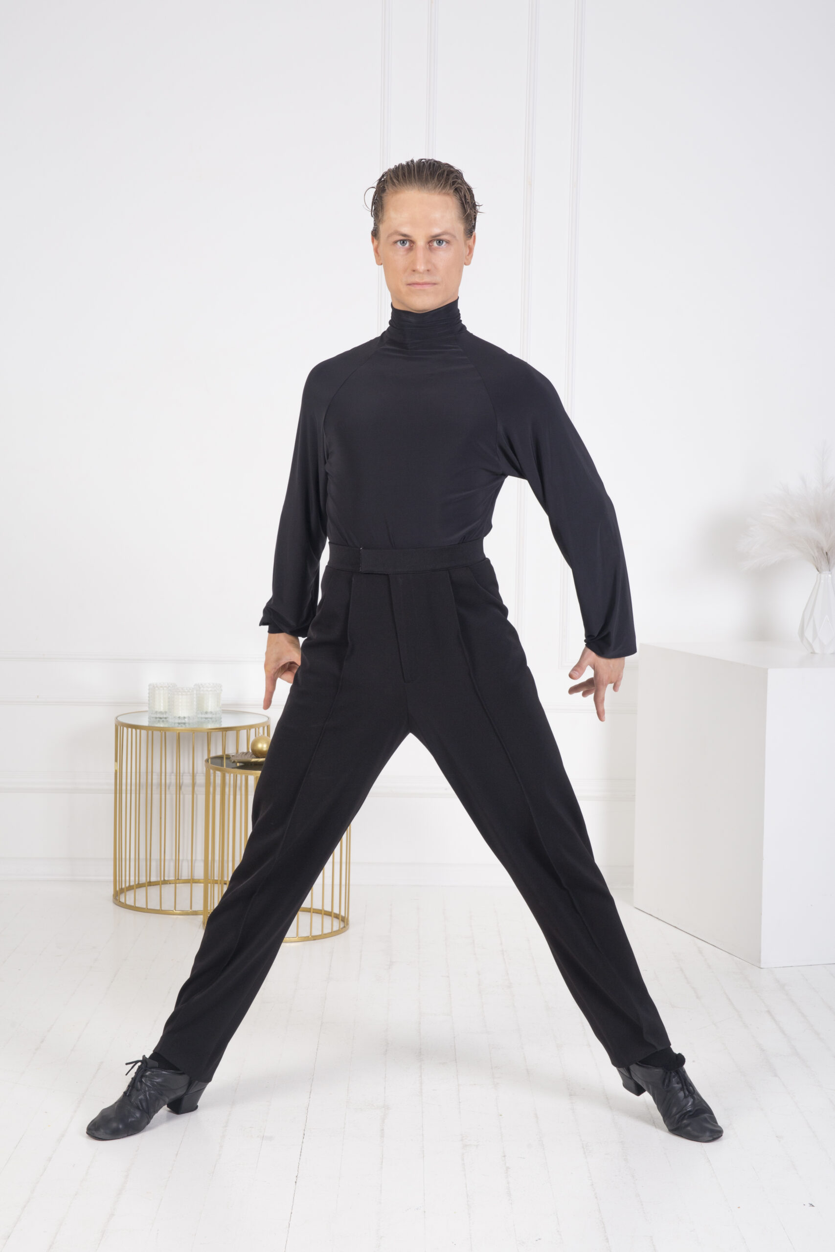 Man in black dancewear striking a pose in a bright studio.